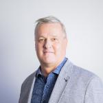 Harmaaseen pikkutakkiin pukeutunut Kimmo katsoo suoraan kameraan.