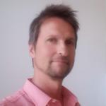 Vaaleanpunaiseen kauluspaitaan pukeutunut Janne katsoo suoraan kameraan.