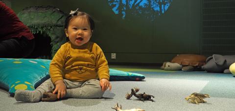 Taapero istumassa Rullan elämystilan lattialLittle child sitting on Rulla's Terra-space with little plastic animal toys.