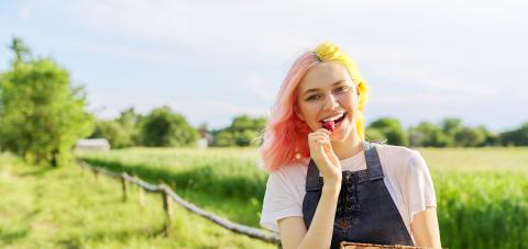 Henkilö kävelee pellon laidalla mansikkakori kädessään. Hän haukkaa yhtä mansikkaa.