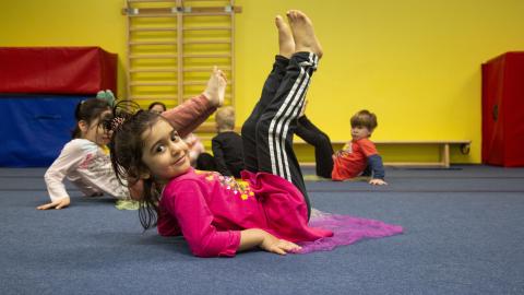 Pikkutyttö makaa jalat kohti kattoa jumppa-alustalla.