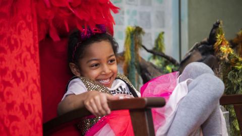 Child sits on a red chair and laughs.