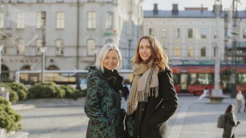 Maiju Viiki and Anna-Kaisa Heinämäki are standing at Tampere Central Square with a tram and a bus in the background.