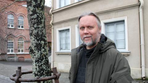 Mies seisoo puun vieressä takki päällä.