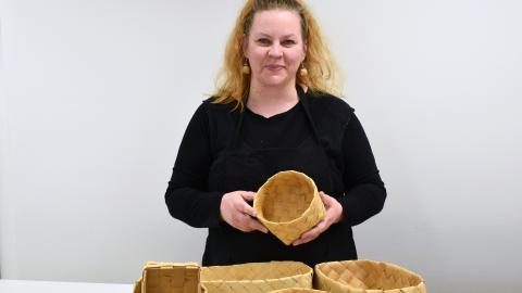 Henkilö pitelee tuohitöitä käsissään. Etualalla koreja.