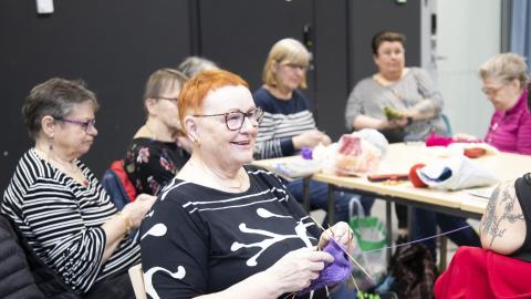 Aulikki istuu salissa neulomassa käsitöitä käsityökerhon kanssa.
