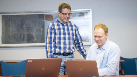 Paikkatietoasiantuntijat katsovat kannettavan tietokoneen näyttöä kokoushuoneen pöydän ääressä.