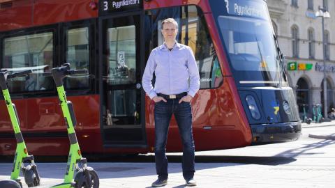 Henkilö seisoo ratikan edessä kadulla. Viereen on jätetty sähköpotkulautoja.