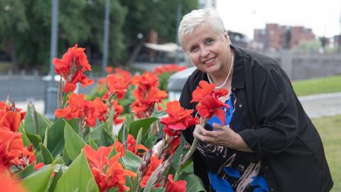 Henkilö seisoo kukkien vieressä ja katsoo kameraan.