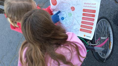 Kaksi koululaista tutkii karttaa, kuvassa polkupyöriä.