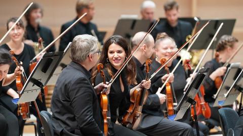 The Tampere Philharmonic Orchestra's musicians sitting with their instruments in the concert hall, María Garcia in the middle.