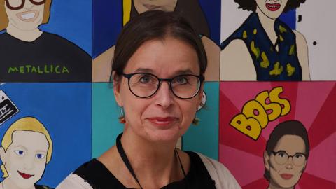 Rehtori Tuija Ylöniemi kuvattuna itseään esittävien maalattujen kuvien koostetaulun edessä.