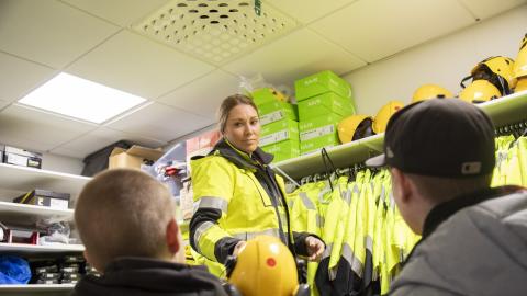 Ohjaaja ojentaa toiselle selin istuvista opiskelijoista kypärän.