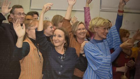 Henkilöt seisovat kädet ylhäällä ja tanssivat.