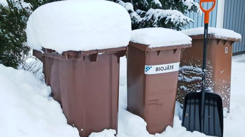 Pihalla lumisia jäteastioita ja lumilapio.