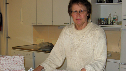 Henkilö seisoo opetuskeittiössä. Taustalla on tiskiallas, ja pöydällä on viikattuja liinoja.