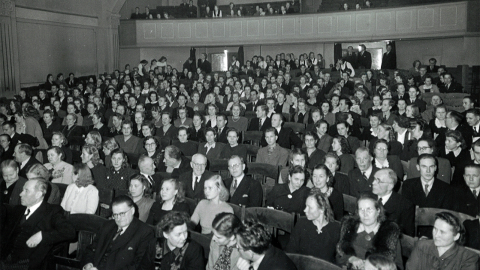 Henkilöistä suuressa luentosalissa, jonka takana on parvi.