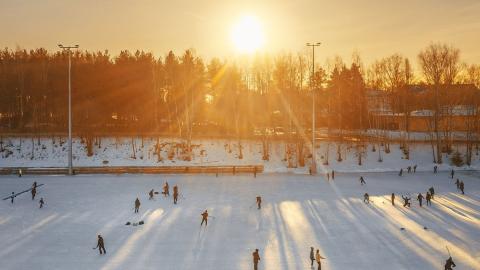 Luistelijoita Sorsapuiston tekojäällä, aurinko paistaa matalalta.