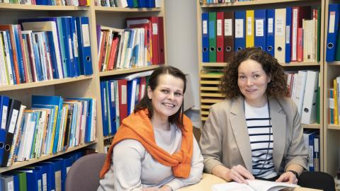 Two people are sitting at a table in front of a full bookcase.
