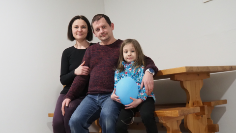 Kolmihenkinen perhe istuu pöydän äärellä. Lapsella on kädessä sininen ilmapallo.