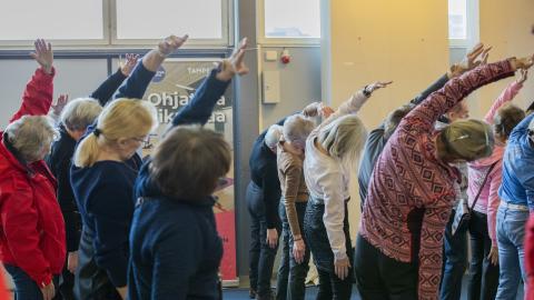 Senioreita osallistumassa liikuntatuokioon ja jumppaamassa seisten.