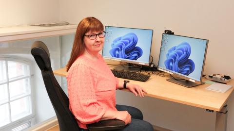 Henkilö istuu työpöydän ääressä ja katsoo kameraan.