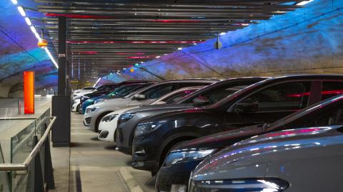 Henkilöautoja rivissä parkkihallissa, jonka harmaille tunneliseinämille heijastuu sinisen eri sävyjä.