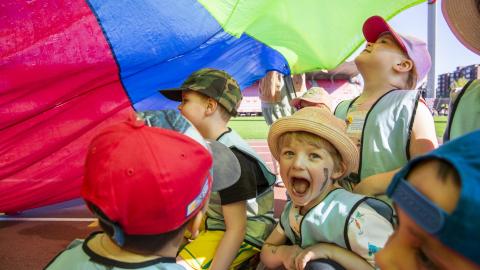 Hattupäisiä lapsia värikkään kankaan kanssa.