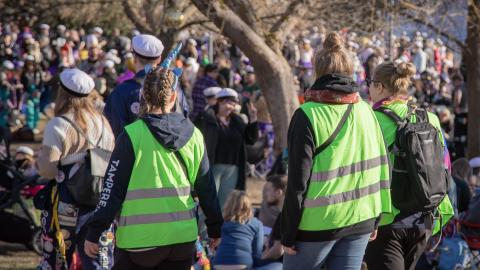 Kolme vihreäliivistä henkilöä kulkee juhlijoiden joukossa ulkona.