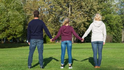 Vanhemmat ja nuori kulkevat käsi kädessä poispäin katsojasta.