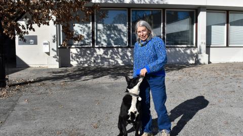 A person stands in front of the school with their dog. The dog sniffs the owner's hands.