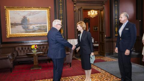 Kaksi henkilöä kättelee. Heidän oikealla puolellaan seisoo kolmas henkilö.