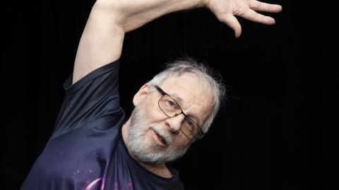 Man against the black backround, his left hand aroused over his head.