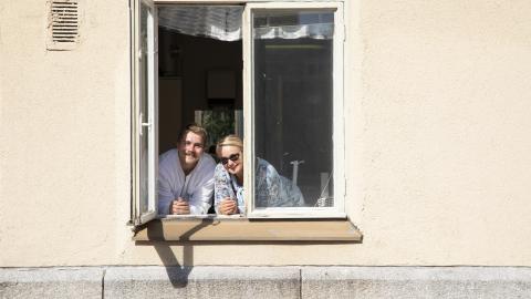 A man and a woman peer out of the window of a light-coloured building.