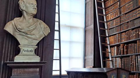 A library building with one wall filled with books and a statue on the left side.