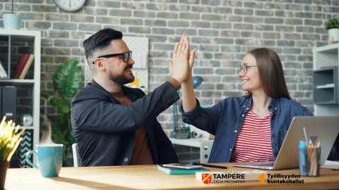 Vanhempi työntekijä ja nuori hymyilevät ja paiskaavat kättä läppärin äärellä.