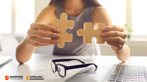 Nainen istuu pöydän ääressä. Hän sovittaa kahta isoa palapelin palaa käsissään yhteen.