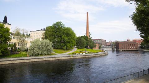 A river. On the backround pale yellow buildings on the left, a chimney in the center and red brick buildings on the right.