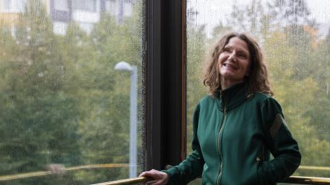 Vihreäasuinen henkilö poseeraa ikkunaa vasten.