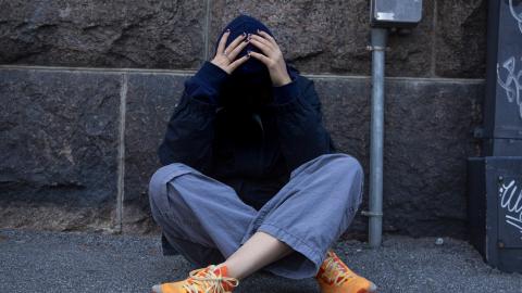 Young person is sitting on the ground holding their head.