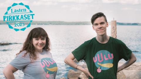 Two persons standing by the lake and smiling at the camera. At the top right, the text Lasten Pirkkaset 2025.