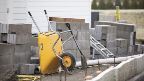 Keltaiset kottikärryt ja lapio harkkotiilien joukossa rakennustyömaalla. 