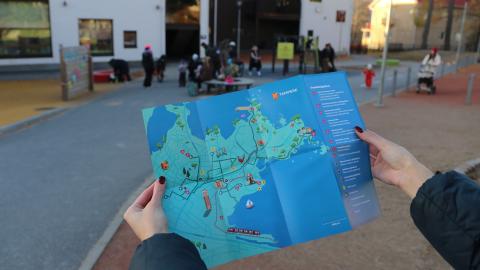 Seikkailukartta lähikuvassa, taustalla päiväkodin pihassa vilskettä.