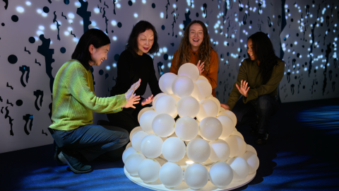 Four people are stood around a large, white snow lantern, interior image of the Moomin Museum.