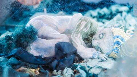 Valkean värinen nukketeatterinukke makoilee sinisen kankaan päällä.