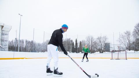 Etualalla seisova pelaaja on syöttämässä kiekkoa maalin lähellä seisovalle toiselle pelaajalle.