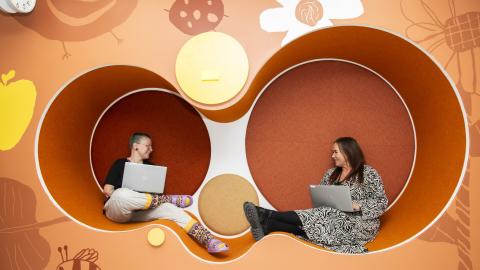 Varhaiskasvatuksen opettaja Ruska Lönn (vasemmalla) ja päiväkodin johtaja Marika Pihkanen istuvat vastakkain päiväkodin leikkitiloissa tietokoneet käsissään ja juttelevat toisilleen..