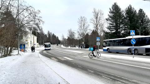 Kuvassa katua, busseja ja bussin odottajia, pyörälijä.