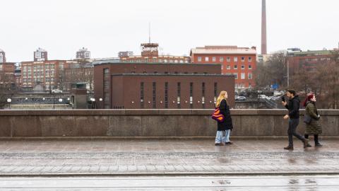 Kolme henkilöä kävelemässä vastakkaisiin suuntiin Hämeensillalla, taustalla Tammerkosken putous ja voimalaitos.