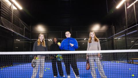 Four people stands on the padel court behind the net.